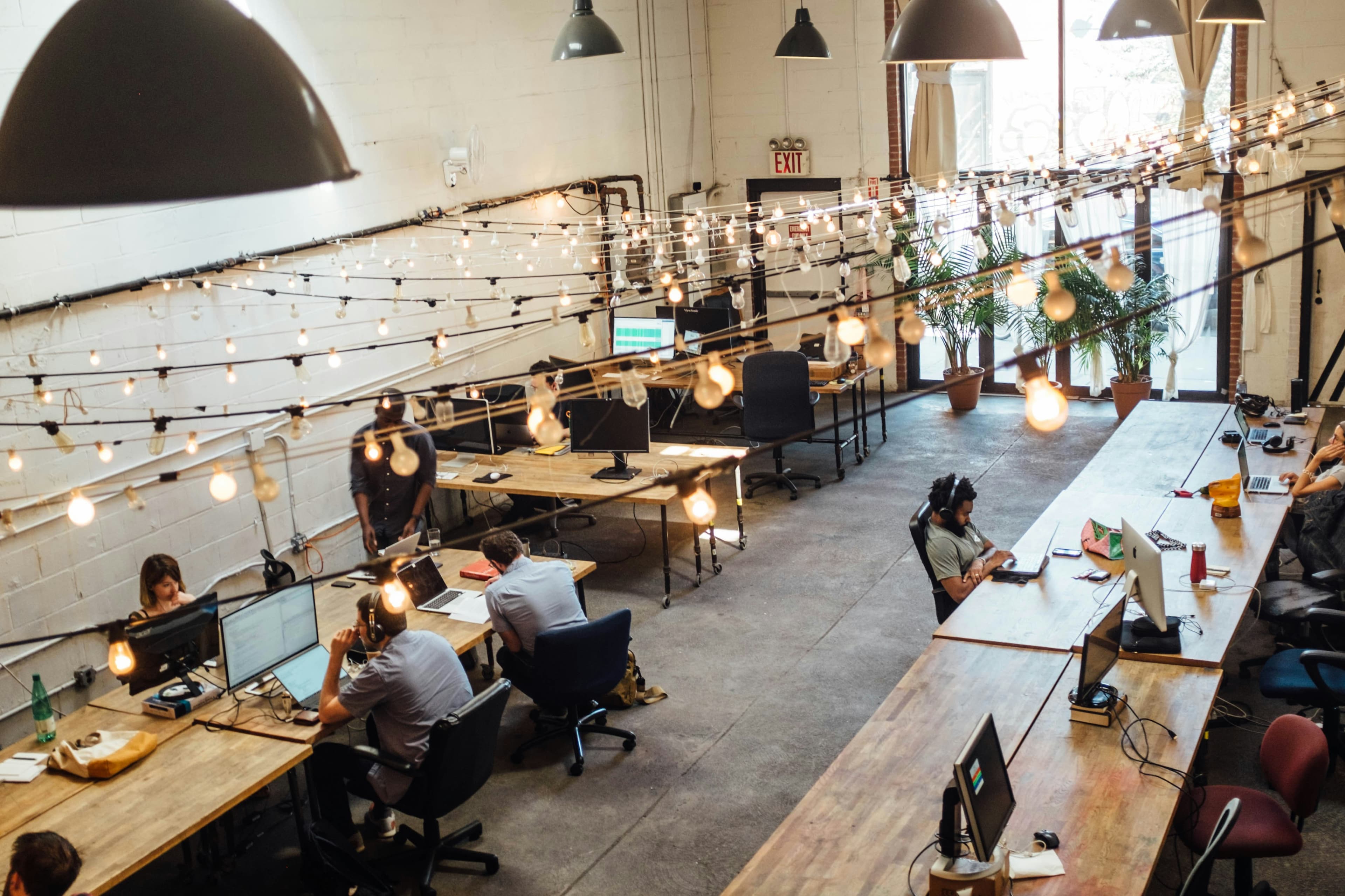 Espace de coworking avec plusieurs personnes travaillant à des bureaux partagés, sous un plafond décoré de guirlandes lumineuses.